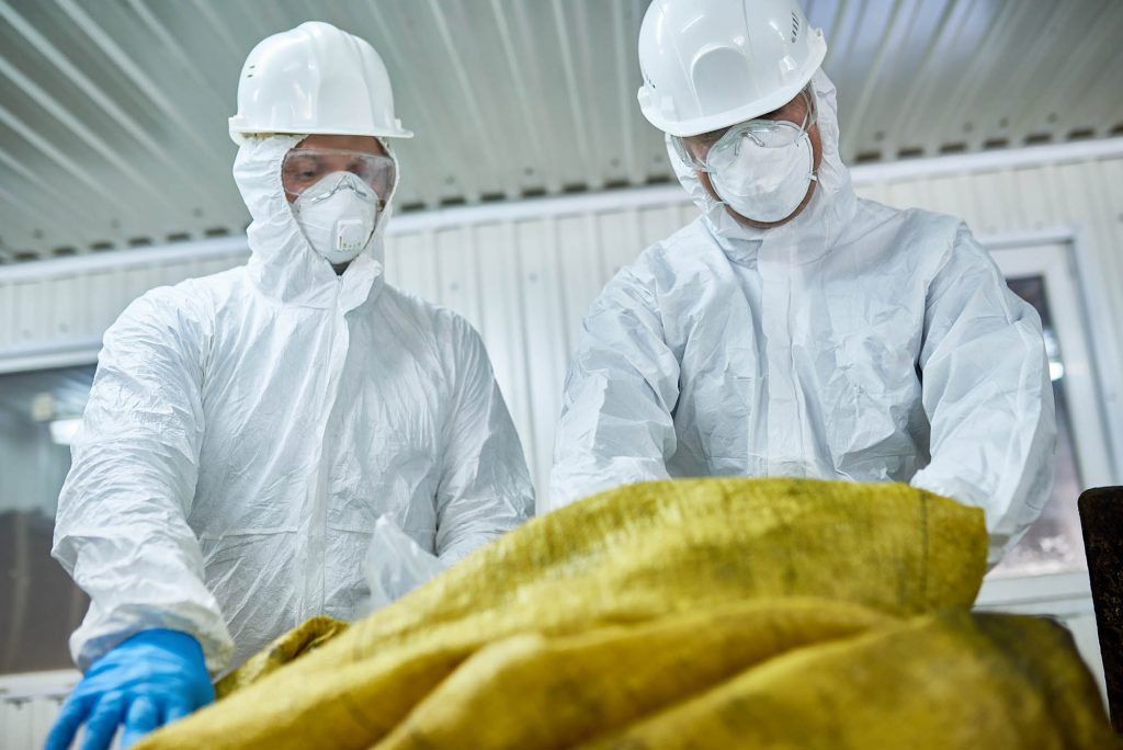 Waste management workers wearing biohazard suits working at waste processing plant sorting recyclable materials on conveyor belt